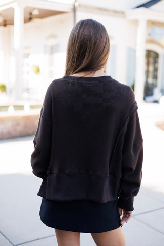 Back view from the waist up showcasing the relaxed fit and slouched drape of the dark brown thermal waffle sweater. Details include dropped sleeve seams, textured waffle-weave cotton fabric, and a wide ribbed bottom band.