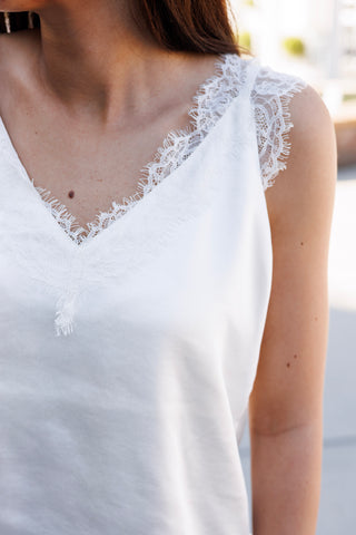 Macro shot focusing on the delicate eyelash lace scalloped trim along the V-neckline of the white satin camisole. Highlights the fine eyelash lace eyelash texture and clean seam construction.