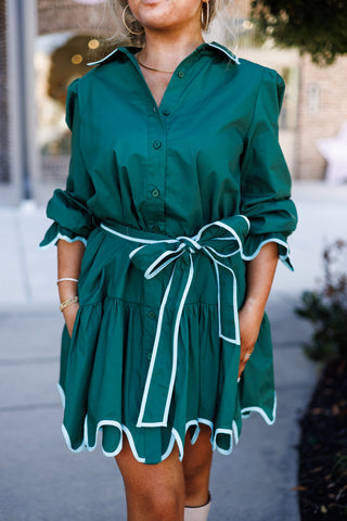 Close-up view focusing on the waist and skirt construction of the Emerald Scalloped Shirt Dress. Highlights the tied bow sash belt, button placket, and wavy scalloped bottom hem lined with light blue piping.