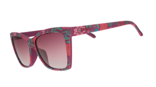 Angled side view of the Goodr Prairie Mystique Fuschia Fields Forever sunglasses against a transparent background. This perspective highlights the continuous floral pattern extending seamlessly down the temple arms, which features the classic "goodr" logo embedded in raised pink text. The view also reveals the solid fuchsia inner frame edge and showcases the subtle curve of the pink gradient lenses.