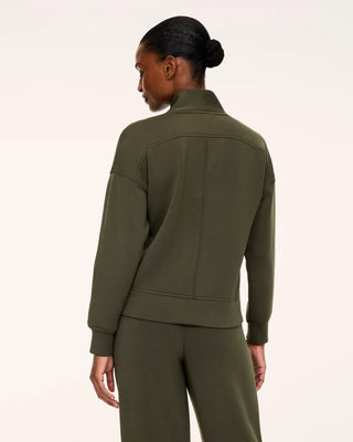 Back view of the Monstera green AirEssentials long-sleeve pullover showcasing the architectural standing funnel neckline and tailored back yoke stitching. The fluid, ultra-drapey silhouette displays loose-fitting drop shoulders and a smooth horizontal hem band paired with coordinating olive green trousers.