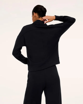 Rear view of the Very Black AirEssentials V-neck pullover, emphasizing the high standing back collar and curved horizontal yoke seam across the shoulders. The structured yet drapey knit fabric features a clean vertical center back seam, drop sleeves, and a defined bottom hem band, styled with coordinating high-waisted black lounge pants.