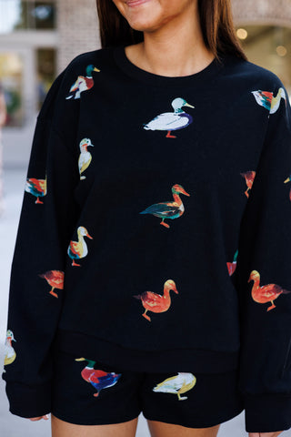 Portrait shot of the black crewneck sweatshirt displaying the detailed watercolor duck print in vibrant shades of mallard green, rusty orange, blue, white, and yellow. Features a classic ribbed crew collar, dropped shoulder seams, and relaxed long sleeves.