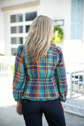 Back view of the long-sleeve teal plaid blouse, showcasing the fitted elastic smocked waistband that creates a gentle peplum flare at the hem. The multicolor plaid pattern in teal, purple, orange, and gold stretches across the upper back and long puff sleeves with elastic cuffs, paired with dark wash denim pants.