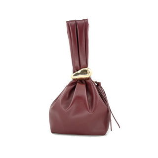 Front view of a deep burgundy smooth leather-look pouch bag set against a crisp white background. The handbag features a soft, slouchy base that is elegantly cinched at the neck by a striking, sculptural gold-tone ring, creating a thick, gathered upright top handle. Delicate, matching leather tie details hang gracefully from the side of the cinched closure, completing this modern, architectural accessory.