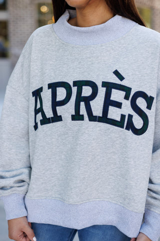 Close-up view focusing on the chest text of the light heather grey fleece pullover. Displays the rich texture and navy embroidered border of the green and navy tartan plaid "APRÈS" fabric appliqué, as well as the thick ribbing along the high collar and lower hem.