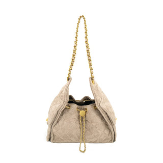 Front view of a slouchy taupe quilted suede handbag set against a crisp white background. The bag features a plush diamond-stitched pattern, relaxed winged side panels, and a softly cinched top secured by a gold-tone chain drawstring with a smooth, round gold slider. A woven gold-tone chain and faux-leather shoulder strap extends upward, completing the elegant, textural silhouette.