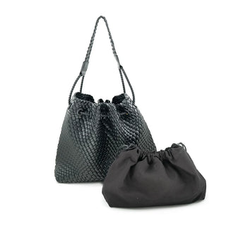 A stylish black woven bucket bag featuring a braided shoulder strap and a cinched drawstring closure at the top. Displayed on a crisp white background, the textured handbag is paired with a soft, solid black fabric drawstring pouch resting just in front of it, completing this versatile accessory set.