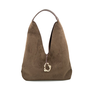 Front view of a rich chocolate brown suede hobo bag set against a crisp white background. The handbag features a relaxed, slouchy silhouette characterized by a deep V-shaped plunge at the top, creating a soft, unstructured look. It is carried by a single smooth, tonal leather top handle and is distinctly accented by a thin leather cord hanging down the center, which holds an organic-shaped, hammered gold-tone ring pendant.