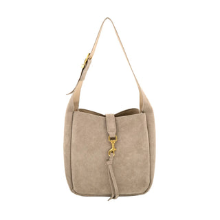 Taupe suede shoulder bag featuring a soft, structured bucket silhouette with smooth tonal trim. The front is accented with a suede tab closure, a polished gold-tone dog-clip clasp, and a hanging suede tassel detail. It includes a thick, adjustable flat shoulder strap attached with gold hardware against a clean white background.