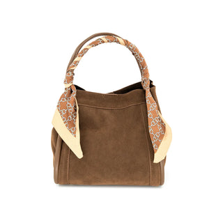 Front view of a rich chocolate brown suede handbag set against a crisp white background. The softly structured silhouette features smooth tonal leather piping details along the front edges and a single, curved top handle elegantly wrapped in a brown and cream chain-link patterned silk scarf. The scarf is tied securely at the base of the handle, with the pointed, cream-bordered ends draped beautifully down the sides of the bag for a chic, accessorized look.