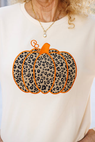 Close-up view of the sweatshirt's chest art showing the intricate embroidery and texture of the animal-print pumpkin graphic. Features a tan and black leopard spot fabric filling, outlined with bold orange stitched borders, an orange stem, and a delicate curly vine flourish on soft cream fleece fabric.