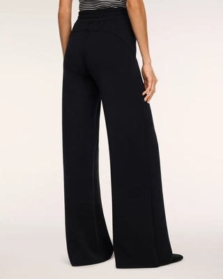 Rear view of the Very Black AirEssentials wide-leg pant showcasing the contouring curved back yoke seam and subtle elasticized ruched waistband. The fluid, ultra-soft knit fabric drapes effortlessly through the hips into a relaxed, floor-grazing straight wide-leg silhouette, styled with sleek black flats.   