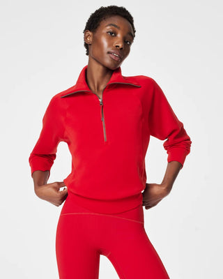 Front view of a model wearing a vibrant crimson red half-zip athletic pullover sweatshirt paired with matching ribbed high-waisted leggings. The pullover features an oversized fold-down funnel collar with an antique silver zipper closure, relaxed raglan drop-shoulder sleeves with subtle slit cuffs, and a ribbed band hem hitting at the waist against a crisp white studio background.