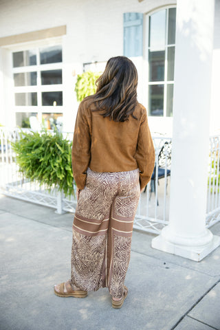 Close-up back view of a woman wearing a sleeveless tiger print mini shift dress, highlighting the structured tailoring and visible exposed back zipper closure running down the center spine. The neutral animal print pattern in shades of cream, beige, and charcoal shows clean paneling details. Styled with stacked gold bangles and her brunette hair worn in soft waves.