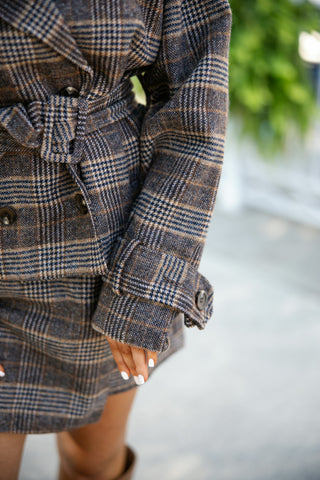 Extremely detailed close-up shot focusing on the sleeve cuff of the plaid trench jacket, featuring a button-tab wrist detail, dark brown tortoise buttons, and the rich brown, navy, and tan wool-look woven pattern.