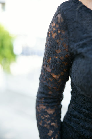 A close-up side detail shot highlighting the intricate floral lace design and semi-sheer sleeve texture of a black long-sleeve lace maxi dress, demonstrating the sheer contrast overlay on the arm.