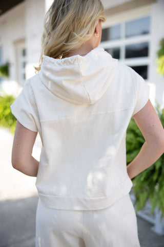 Back view of the French Vanilla Set top, showing the relaxed drape of the solid cream short-sleeve hoodie. The image highlights the hood resting naturally on the upper back and a clean horizontal back yoke seam that complements the comfortable, boxy silhouette.