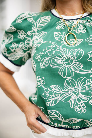 A detailed close-up shot of the Emerald Vine Blouse focusing on the high-quality woven fabric and intricate white leaf and flower embroidery. The image highlights the athletic-inspired navy and white striped ribbed knit band at the neckline and cuffs, complete with a unique white fringe ruffle edge. The structured shoulder gathers of the puff sleeve are clearly visible, paired with a delicate gold chain necklace spelling out letters and a large oval gold pendant.