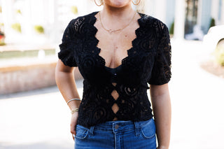 Close-up view of the black paisley lace top highlighting the scalloped V-neck line, sheer lace detail on the short puff sleeves, and textured openwork lace fabric.