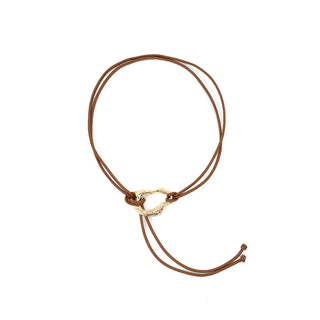 Front view of a minimalist tan cord wrap belt or lariat necklace set against a crisp white background. The versatile accessory features a double strand of smooth, thin tan cording that secures by gracefully looping through an asymmetrical, organic-shaped hammered gold-tone central ring. The long cords trail elegantly below the metallic hardware, finishing with small, simple knotted details at the tips to complete the modern, bohemian aesthetic.