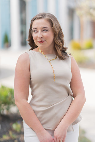 A portrait-style close-up highlighting the architectural details and premium matte finish of the Jayleen Knot Top. The shot emphasizes the clean-finished boat neckline and the soft ruching created by the side-knot detail. The model’s gold lariat necklace serves as a focal point, drawing attention to the top's smooth, high-density jersey fabric and sophisticated taupe hue.