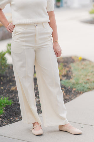 A detailed front view of the Sandbar Stroll Wide-Leg Pants highlighting the impeccable tailoring and structured high-rise waist. This shot showcases the clean zip-fly, subtle button closure, and functional integrated side pockets. The premium mid-weight woven fabric is visible, offering a smooth, wrinkle-resistant finish and a soft, professional drape.