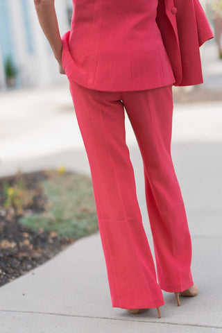 A close-up back view of the Watermelon Sugar Pants showcasing the clean, uninterrupted lines of the high-quality fabric. The generous hemline is visible, tailored to accommodate heels or platform sandals while maintaining a crisp, professional structure. The vibrant "Watermelon Sugar" coral color radiates confidence and warmth.