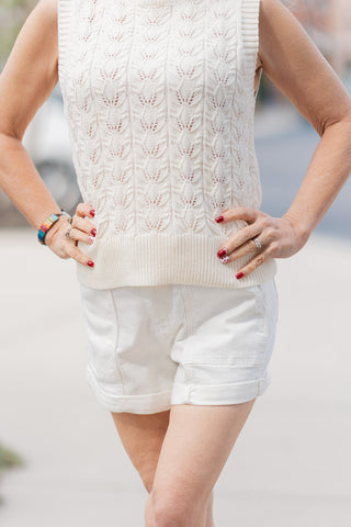 A front close-up view of the Judy Blue Aurora Weekender Shorts, highlighting the high-waisted silhouette and the stylish cuffed hemline. The subject’s hands are placed on her hips, showcasing the functional front pockets and the opaque, premium white denim. The textured, leaf-patterned knit of her cream top is visible tucked into the waistband.