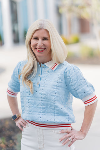 A portrait view showcasing the intricate details of the Court Club Polo. This shot highlights the soft powder blue pointelle fabric with its floral-inspired openwork patterns and the three sparkling, rhinestone-embellished buttons at the front placket. The crisp white collar and striped sleeve cuffs add a preppy, refined touch to the feminine silhouette.