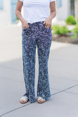A detailed front view of the Midnight Meadow Pants highlighting the intricate leaf and vine botanical pattern. The woman has her hands in the functional side pockets, showcasing the smooth, elasticized waistband and the fluid drape of the lightweight fabric. The high-contrast monochromatic print creates a bold visual texture that is both modern and timeless.