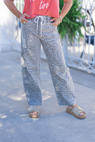 A detailed front view of the Safari Stone Barrel Jeans highlighting the flexible high-rise fit and contrasting white drawstring tie at the waist. The image showcases the subtle stone-grey animal pattern on the breathable mid-weight denim, functional front pockets, and the contemporary curved cut of the barrel leg draping effortlessly over slip-on platform sandals.