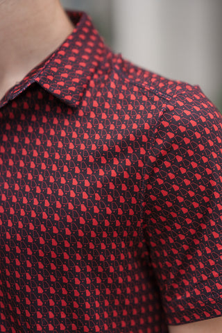 A close-up, angled macro shot showcasing the detailed texture and pattern of the Georgia Performance Polo. The high-quality performance fabric features a repeating geometric state-themed design of vibrant red Georgia outlines and small stars organized in clean rows across a dark maroon background. The stitching along the structured collar, shoulder seam, and short-sleeve hem highlights the sharp, premium craftsmanship of the activewear blend.