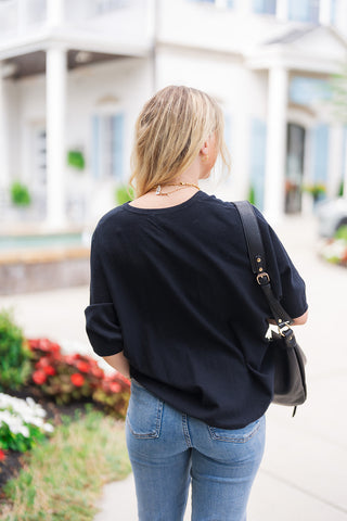 Back view of the Black Cloud V-Neck Top showcasing its seamless rear silhouette and graceful drape over light-wash denim jeans. Highlights the relaxed elbow-length sleeves, soft back neckline, and subtle banded hemline that offers a clean, non-bulky finish ideal for effortless styling.