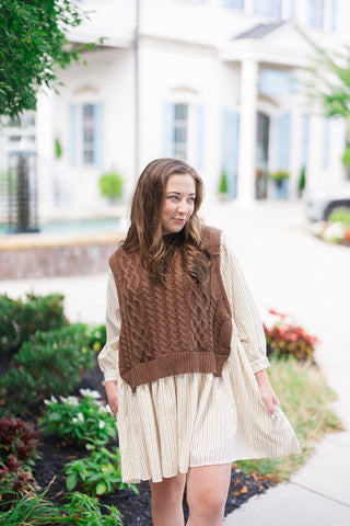 A mid-length front shot of the Chilly Mornings Mini Dress showing the relaxed drape and flared hemline of the pinstriped skirt. The image highlights the contrast between the structured ribbed hem of the cropped brown sweater vest and the flowy, lightweight woven underlayer.