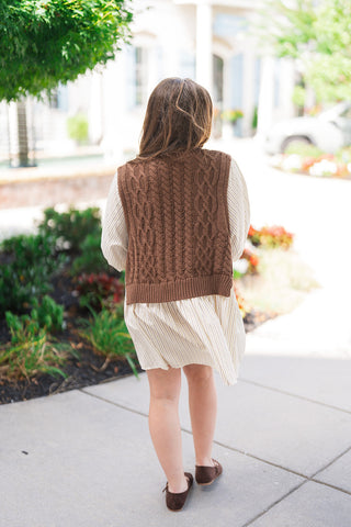 Back view of the Chilly Mornings Mini Dress demonstrating the full cable-knit pattern across the back of the sleeveless brown vest. The shot emphasizes the gentle movement of the pinstriped A-line skirt and the modest coverage provided by the 3/4 balloon sleeves and mini-length hemline.