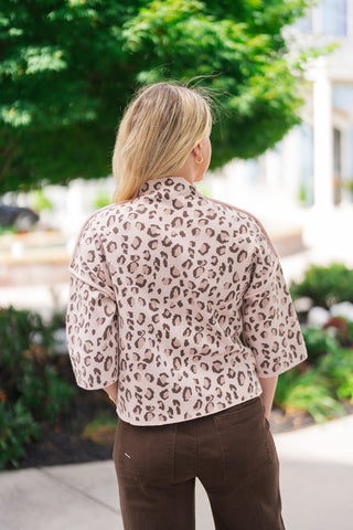 Back view of the Blush Leopard Mock Neck Sweater demonstrating the continuous olive leopard pattern across the back and wide 3/4 sleeves. The shot emphasizes the structured mock neck collar, the clean back drop-shoulder seam, and the straight hem resting over high-waisted dark brown trousers with back pockets.