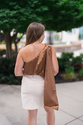 Back view of the Sunset Soirée One-Shoulder Top showcasing the sleek, single-shoulder cut and the floor-length trailing satin sash drape extending down from the right shoulder strap. The shot demonstrates the pleated back design, elasticized hem, and modest open-shoulder back profile.