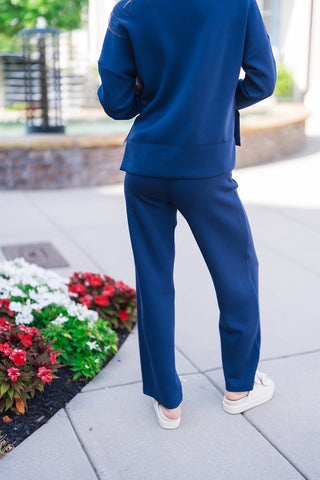 Back view of the SPANX Straight Leg Pants in navy blue showing the comfortable, non-clinging fit across the hips and the straight-leg drape down to the hem. Styled with the matching long-sleeve crewneck top in an outdoor setting.