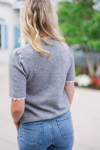 Back view close-up of the Heathered Honey Scallop Knit Top, displaying the subtle puff shoulder construction, soft heathered knit texture, and back crewneck profile with cream scalloped edge detail peeking out. The top sits naturally at the waist over light-wash blue denim jeans.