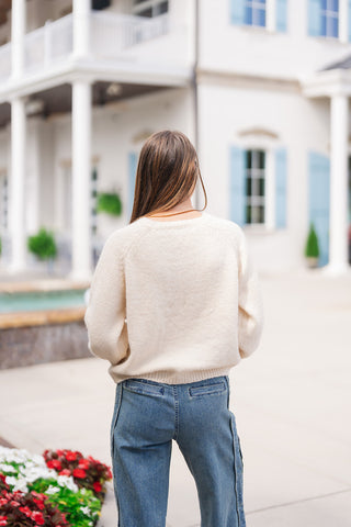 Back view of the Cherry on Top Fuzzy Knit demonstrating the clean, plush texture of the cream eyelash knit across the shoulders and back. The shot emphasizes the relaxed pullover fit, raglan sleeve construction, and subtle ribbed straight hem resting above high-rise blue denim jeans.