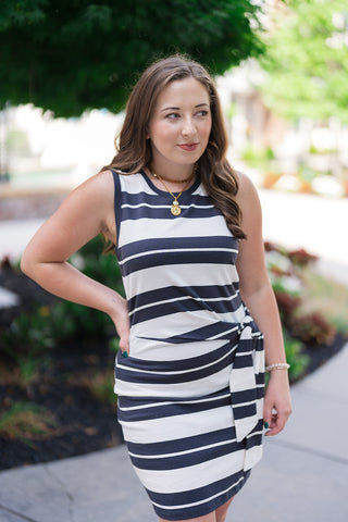 A mid-length front view of the Z Supply Mattie Striped Mini Dress highlighting its sporty sleeveless silhouette and modern high neckline. The soft cotton knit jersey fabric showcases bold, alternating panels of washed ash black and white horizontal stripes. The model is accessorized with a layered gold link and pearl charm necklace, framing the face elegantly.