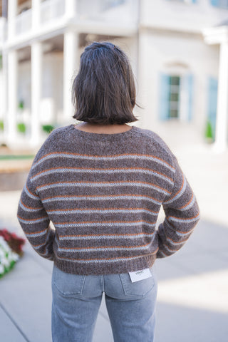 Back view of the fuzzy striped knit sweater highlighting its comfortable drape, continuous horizontal stripe pattern, and soft, mohair-like texture. The relaxed pullover rests at the waistband of light grey denim jeans, which feature classic back patch pockets and a visible white Vervet brand tag on the right side, emphasizing an effortless and trendy seasonal aesthetic.