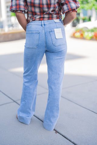 Back view highlighting the tailored fit of the light wash wide-leg denim jeans, showcasing two large, classic back patch pockets and the striking wide hemline at the ankles. The jeans feature a visible white Lovervet by Vervet brand tag attached to the right back pocket, completing a comfortable, vintage-inspired everyday denim look.