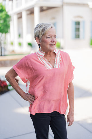 A portrait view of the Sweet Peach Puff-Sleeve Top highlighting the open split V-neckline bordered by delicate cream lace embroidery and a soft cream standing collar. The design showcases the lightweight textured woven fabric in a warm peach tone, relaxed dolman-style cap sleeves, and layered thin gold pendant necklaces.