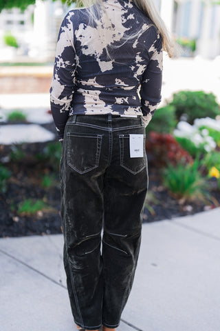 Back mid-body view highlighting the form-fitting silhouette of the black and beige abstract patterned top and its clean tuck into the high-waisted corduroy pants. The dark trousers feature classic back patch pockets and a back yoke, both outlined in bold white contrast stitching that continues down the legs. A visible white Vervet brand sizing tag is attached to the right back pocket, emphasizing a trendy, texture-rich fall aesthetic.
