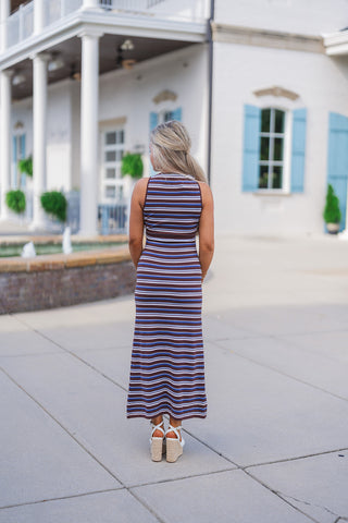 Full body back view of the brown and blue striped maxi dress showcasing its curve-hugging, bodycon silhouette and comfortable stretch fabric. The sleeveless design features a classic high back and falls elegantly to the lower calf, highlighting the continuous horizontal stripe pattern. The dress is paired perfectly with white knot-front espadrille wedges.