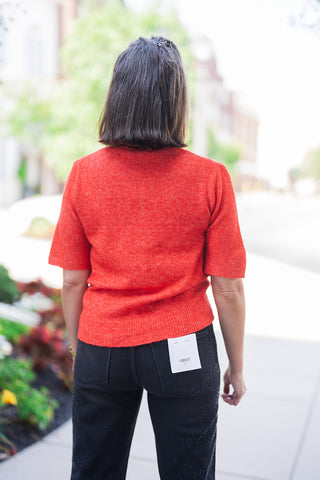Back view showcasing the relaxed yet tailored fit of the vibrant red short-sleeve knit sweater, highlighting its soft texture and classic ribbed hem. The top is paired with black Vervet brand denim jeans featuring classic back pockets and subtle shimmering rhinestone detailing down the legs, with a visible white Vervet sizing tag on the waistband.