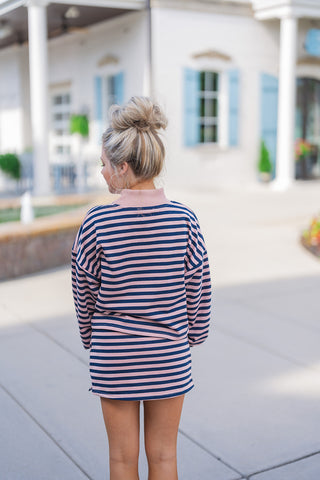 Back view of the navy and pink striped matching set showcasing the comfortable, relaxed drape of the drop-shoulder pullover top. The continuous horizontal stripe pattern flows seamlessly into the matching mini skirt, highlighting a casual, flattering everyday fit. The top features a solid pink ribbed collar that stands out elegantly from the back.