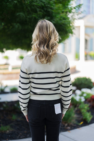 Back view of the Breton Stripe Twist-Front Sweater, showcasing the clean, uninterrupted horizontal black stripes across the cream knit fabric. The long sleeves feature classic ribbed cuffs, and the straight back hem rests cleanly at the waistline of the dark black jeans, offering a versatile, flattering, and modest fit from the reverse angle.